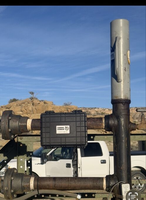 Tubing Tender mounted on wellhead equipment at a field location, white truck visible in the background