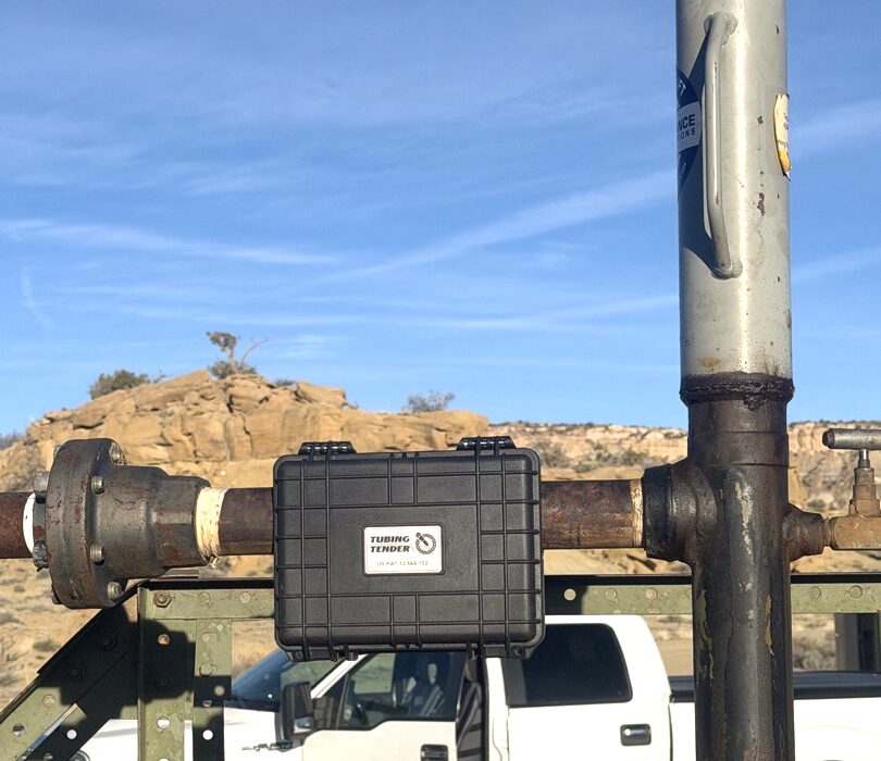 Tubing Tender mounted on a wellhead pipe at a well site in the San Juan Basin, white work truck and desert mesas in the background